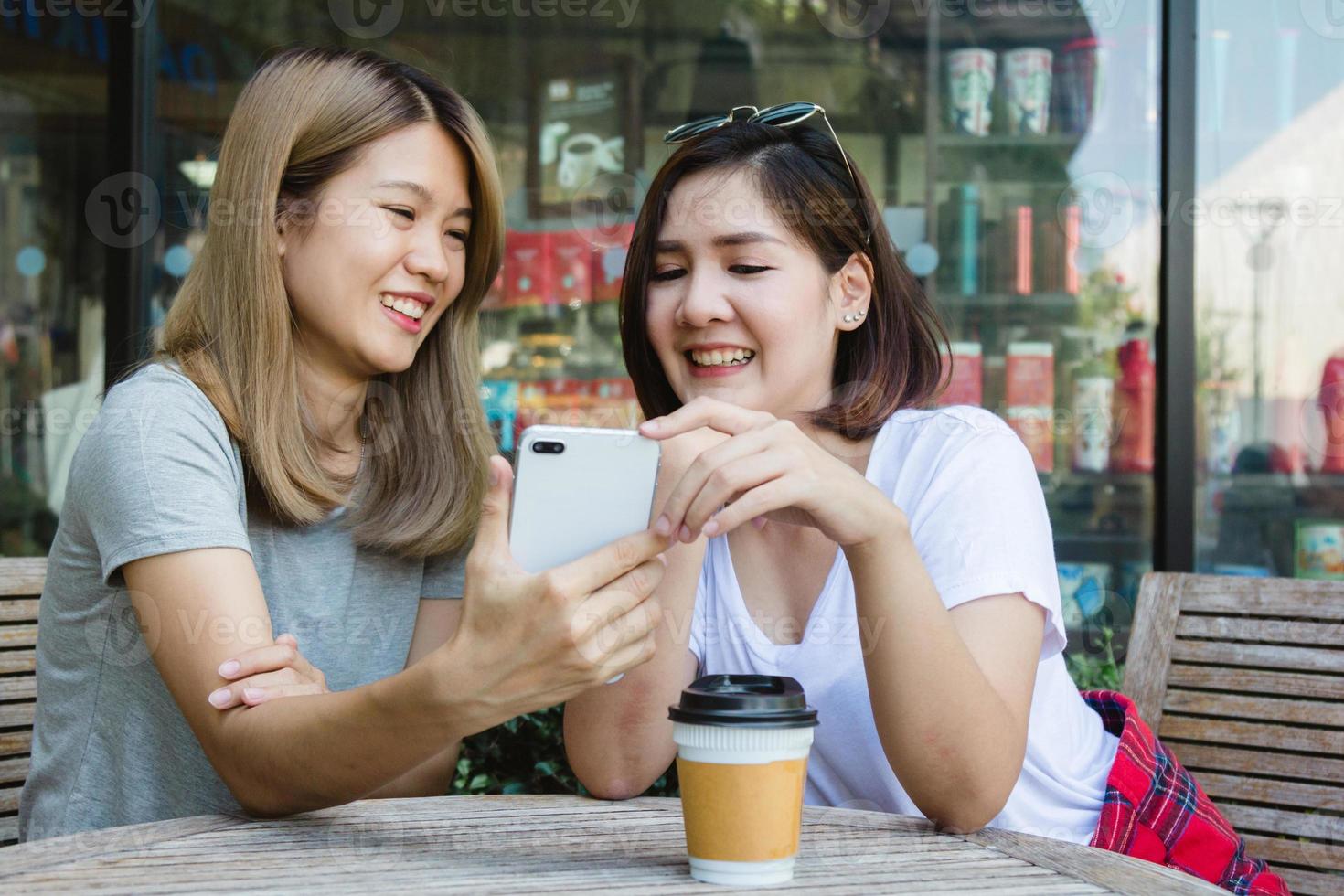 Cheerful asian young women sitting in cafe drinking coffee with friends and talking together. Attractive asian woman enjoying coffee while using smartphone for talking, reading and texting. photo
