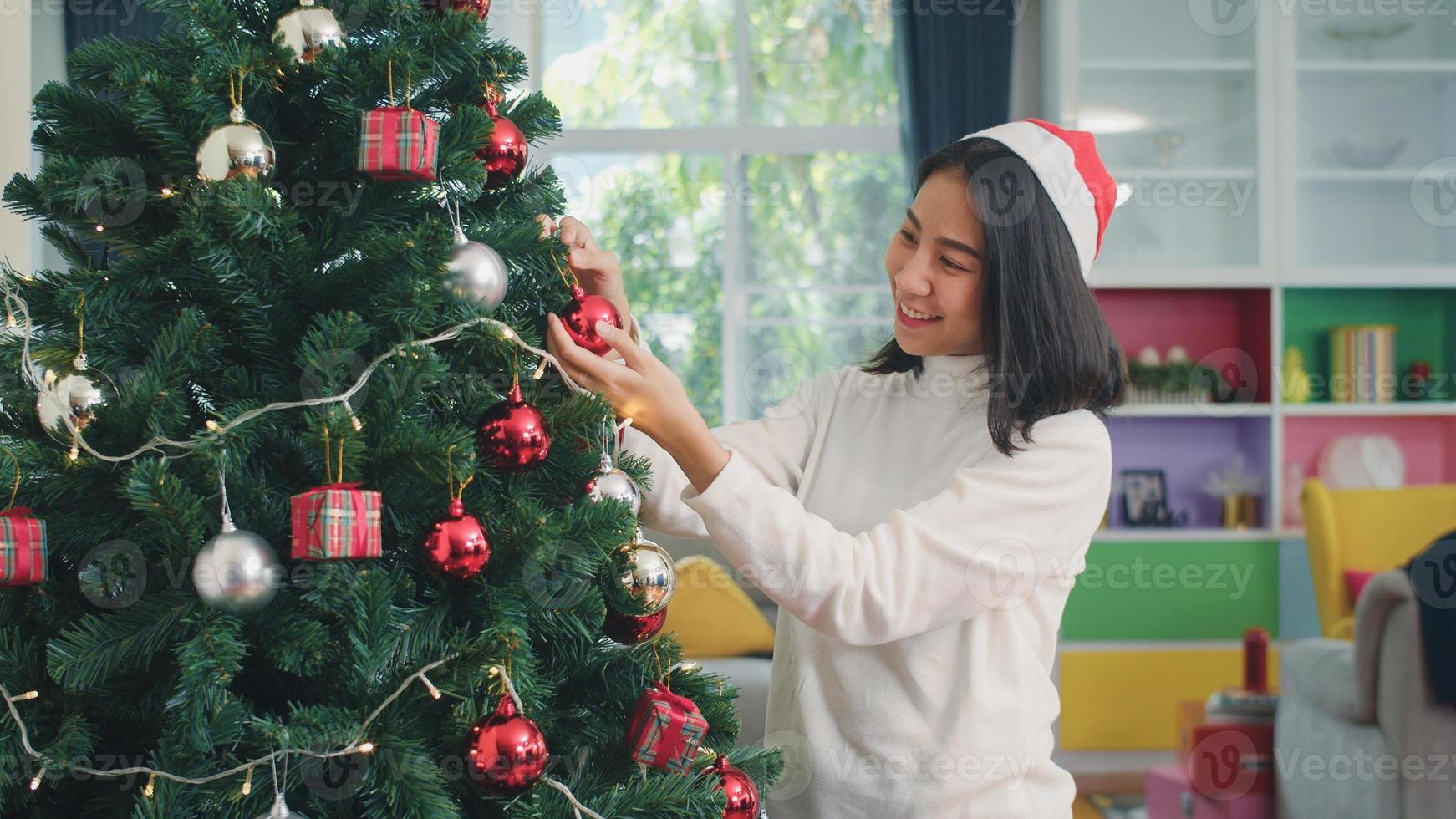 las mujeres asiáticas decoran el árbol de navidad en el festival de navidad. mujer adolescente feliz sonriendo celebrar las vacaciones de invierno de Navidad en la sala de estar en casa. foto