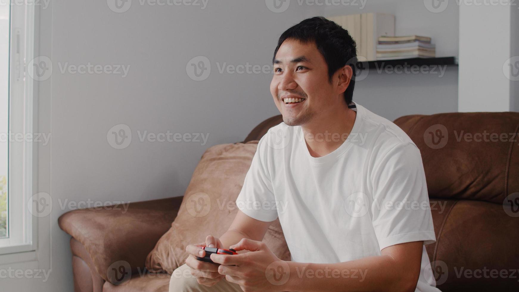 Young Asian man using joystick playing video games in television in living room, male feeling happy using relax time lying on sofa at home. Men play games relax at home concept. photo