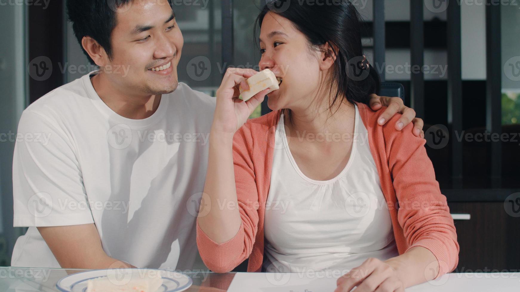 Young Asian Pregnant woman drawing baby in belly and family in notebook. Dad giving sandwich his wife while happy smiling positive and peaceful while take care child on table in living room at home. photo