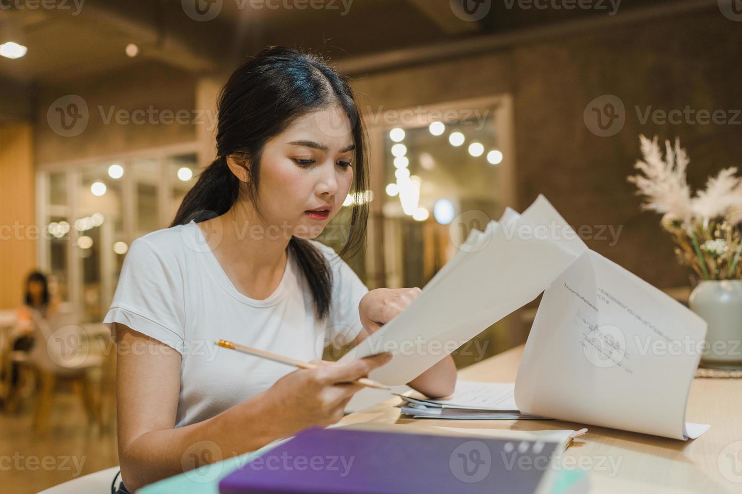Asian student women reading books in library at university. Young undergraduate girl do homework, read textbook, study hard for knowledge on lecture desk at college campus overtime night. photo