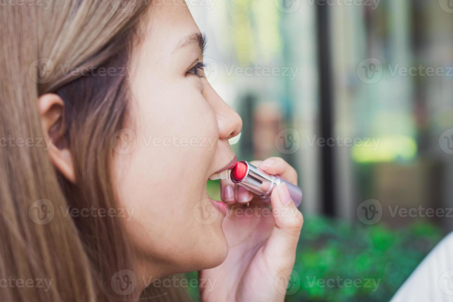 Joven asiática con maquillaje de lápiz labial frente al espejo, mujer feliz con cosméticos de belleza para mejorar, lista para trabajar en el dormitorio en casa. mujeres de estilo de vida en el concepto de hogar. foto