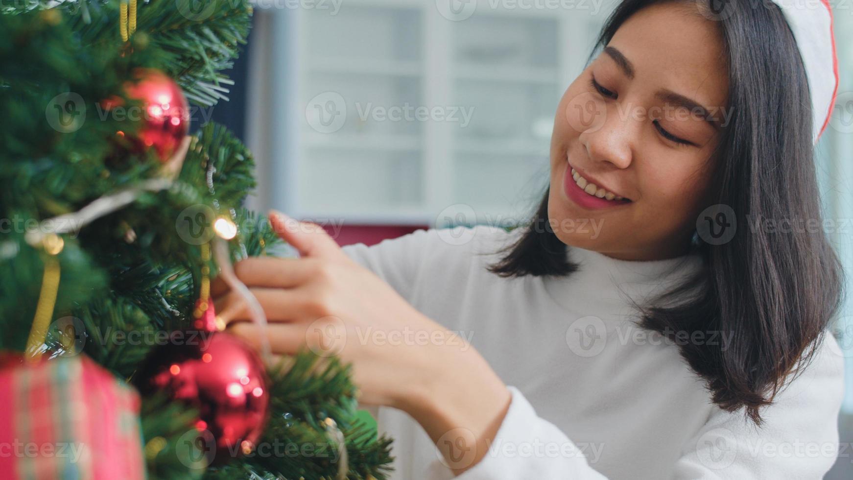 las mujeres asiáticas decoran el árbol de navidad en el festival de navidad. adolescente feliz sonriendo celebra las vacaciones de invierno de Navidad en la sala de estar en casa. fotografía de cerca. foto