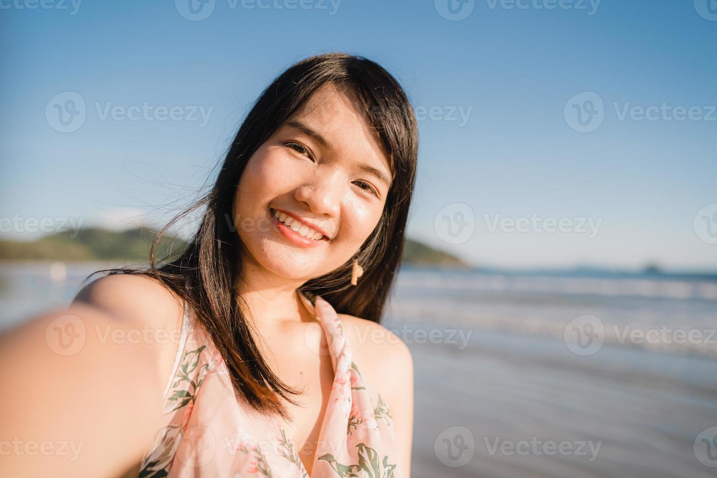 Tourist Asian woman selfie on beach, young beautiful female happy smiling using mobile phone taking selfie on beach near sea when sunset in evening. Lifestyle women travel on beach concept. photo
