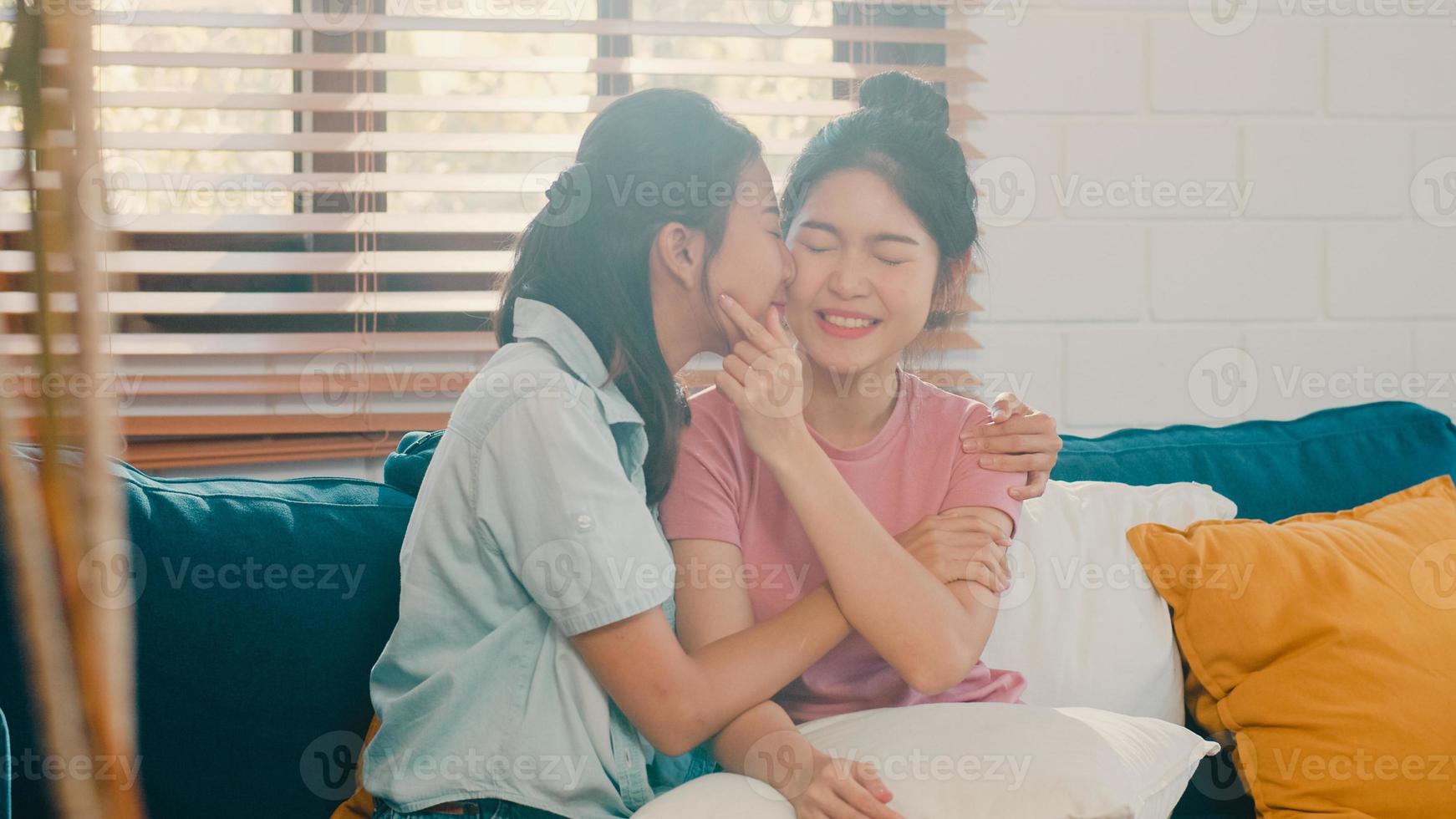 Young Lesbian lgbtq Asian women couple hug and kiss at home. Attractive Asian lover pride female happy relax spend romantic time together while lying sofa in living room concept. photo