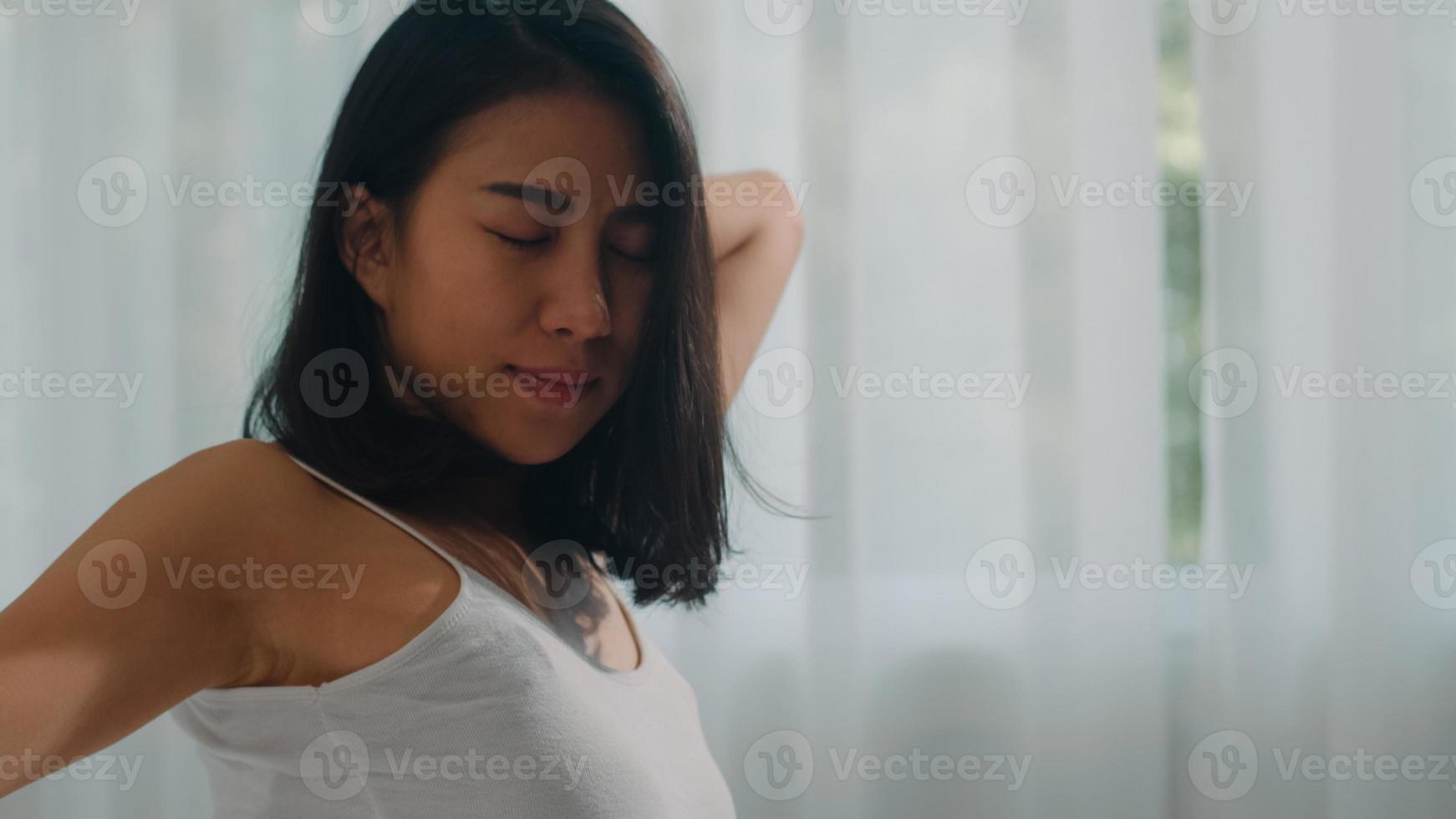 Teen hispanic woman wakes up at home. Young Asian girl stretching after awake sleep all night starting a new day with energy and vitality felt very refreshed on bed near window in bedroom at morning. photo