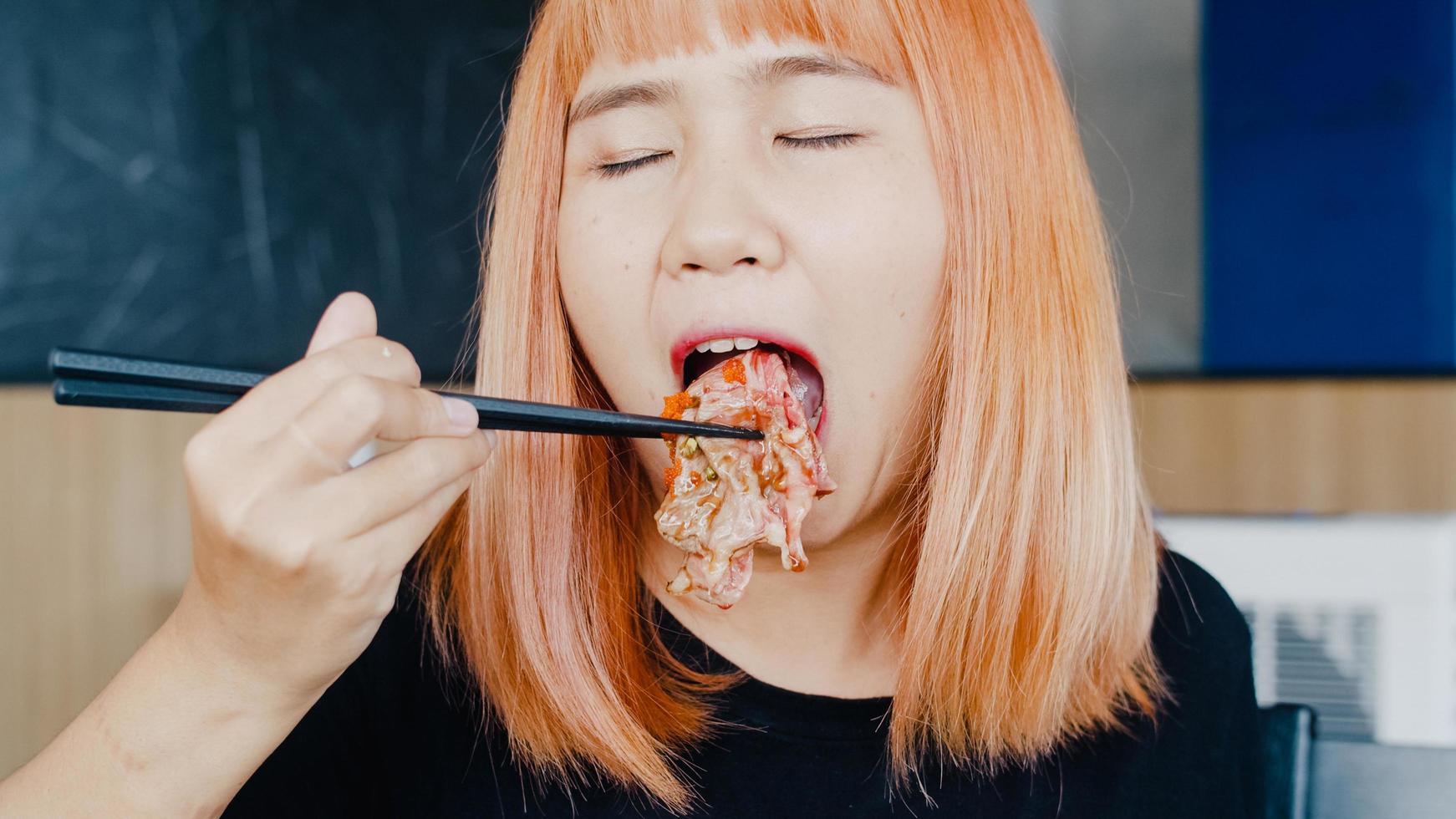 Asian woman eating sushi in japanese restaurant, young female holding chopsticks and eating wagyu beef sushi in lunch time in summer. Lifestyle women eating traditional food concept. photo