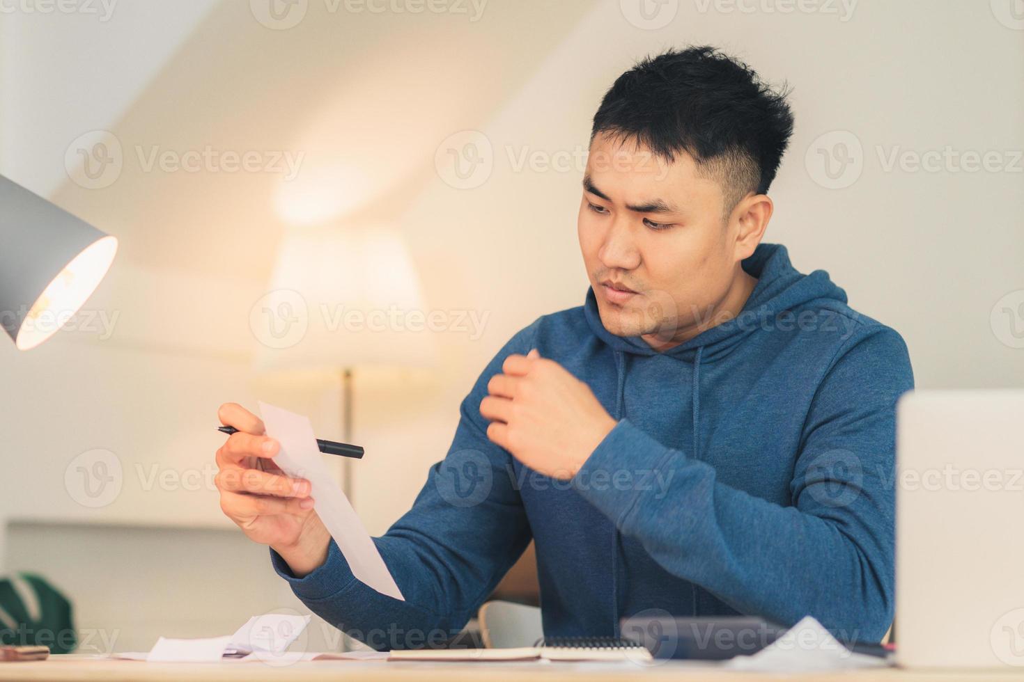 Beautiful young smiling asian man working laptop on desk in living room at home. Asia business man writing notebook document finance and calculator in home office. Enjoying time at home concept. photo