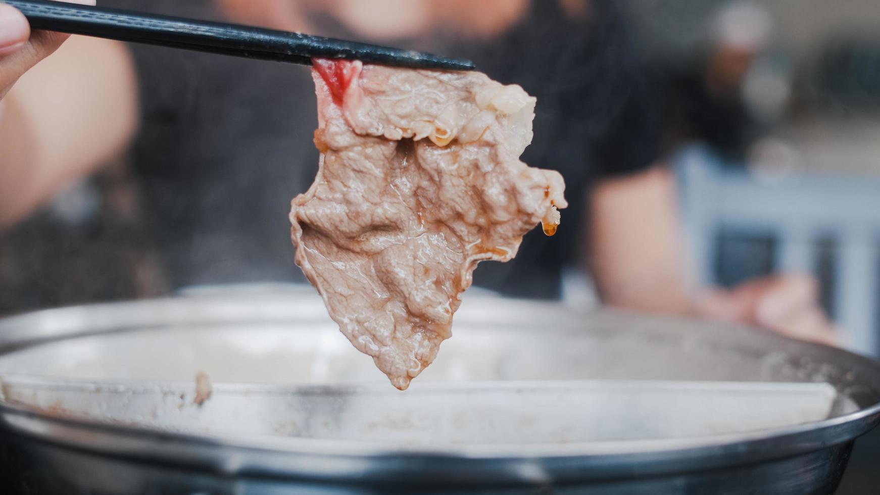 mujer asiática comiendo olla caliente en un restaurante japonés, mujer joven sosteniendo carne de res cortada con palillos come shabu a la hora del almuerzo. mujeres de estilo de vida comiendo concepto de comida. foto