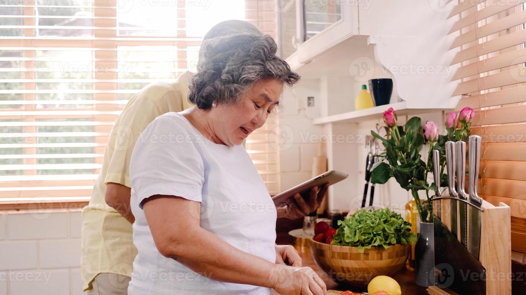 Asian elderly couple cut tomatoes prepare ingredient for making food in the kitchen, Couple use organic vegetable for healthy food at home. Lifestyle senior family making food at home concept. photo