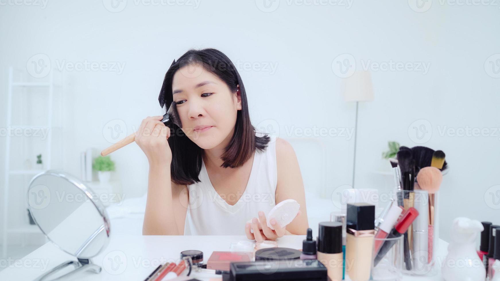 Beauty blogger present beauty cosmetics sitting in front camera for recording video. Happy beautiful young Asian woman use cosmetics review make up tutorial broadcast live video to social network. photo