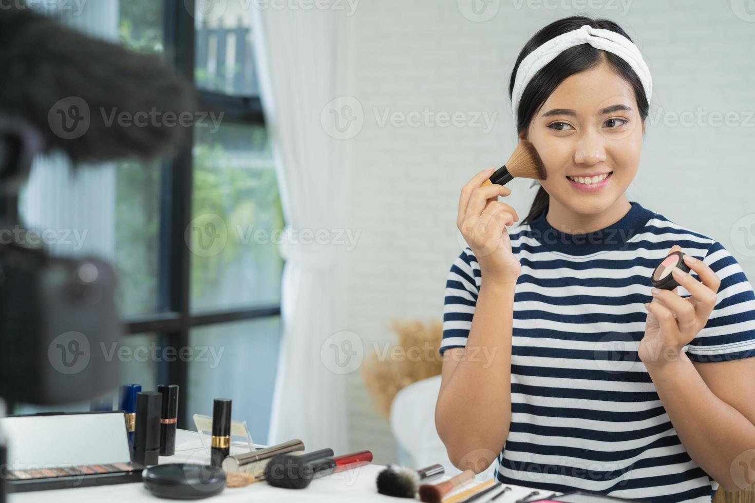 blogger de belleza presenta cosméticos de belleza mientras se sienta frente a la cámara para grabar video. hermosa mujer usa lápiz labial mientras revisa el tutorial de maquillaje transmite video en vivo a la red social por internet. foto