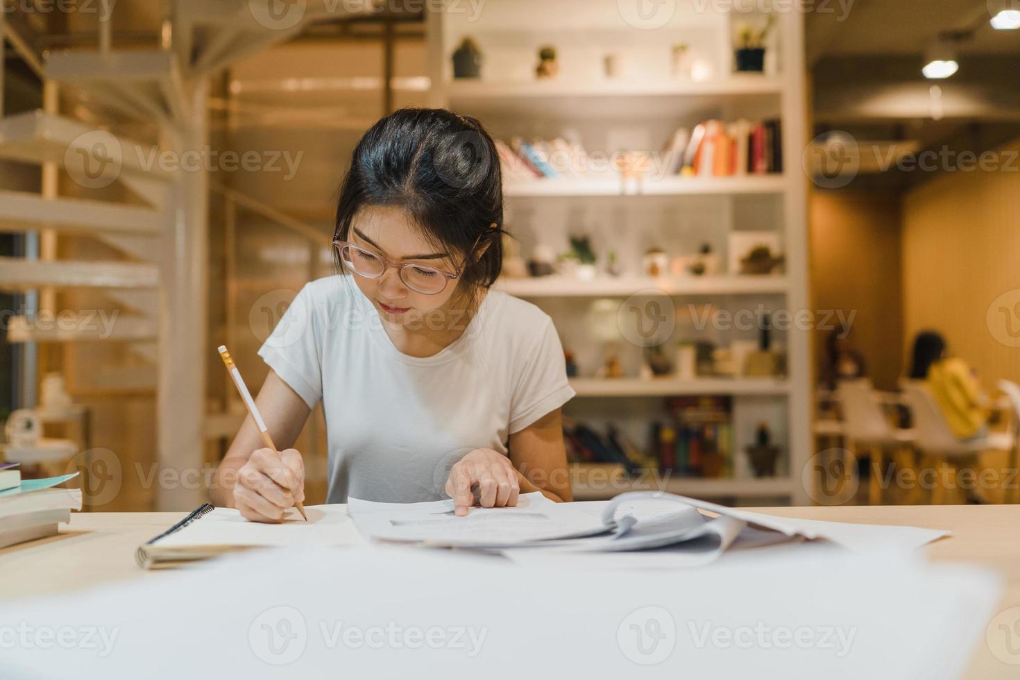 Asian student women reading books in library at university. Young undergraduate girl do homework, read textbook, study hard for knowledge on lecture desk at college campus overtime night. photo