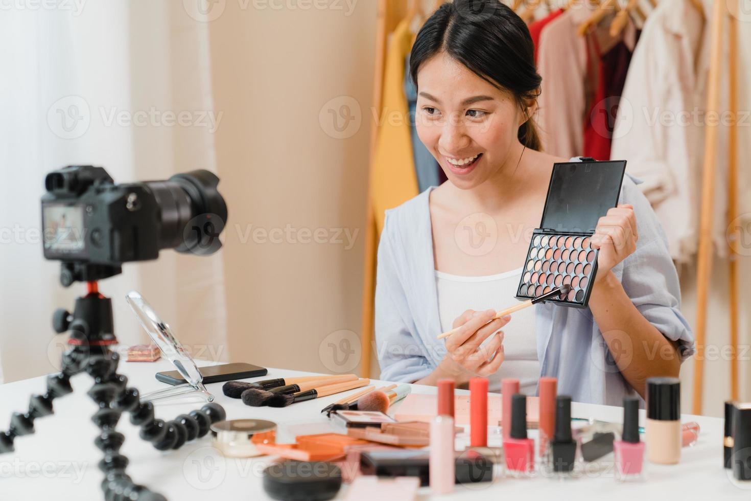 Beauty blogger present beauty cosmetics sitting in front camera for recording video. Beautiful asian woman use cosmetics review make up tutorial broadcast live video to social network by internet. photo