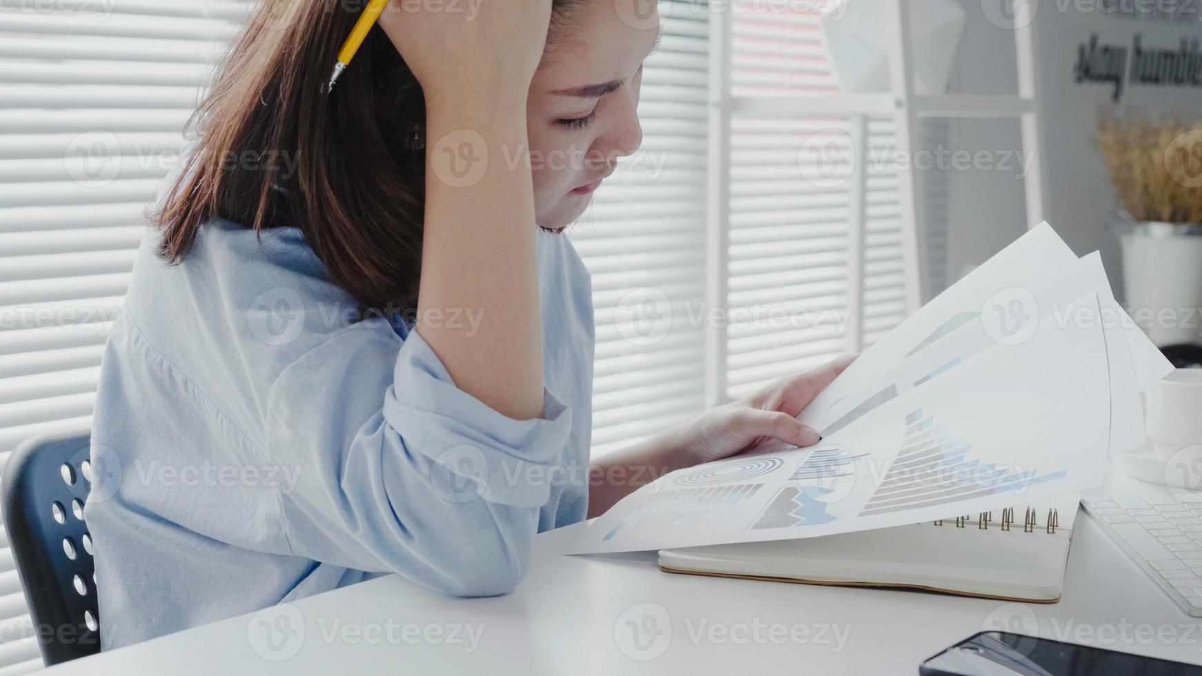 Hermosa joven mujer asiática trabajando en una laptop mientras se sienta en una sala de estar en casa. mujer de negocios asiática que trabaja en su oficina en casa. foto