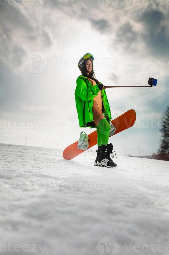 Beautiful woman using smartphone to making selfie with a snowboard on a ski slope photo