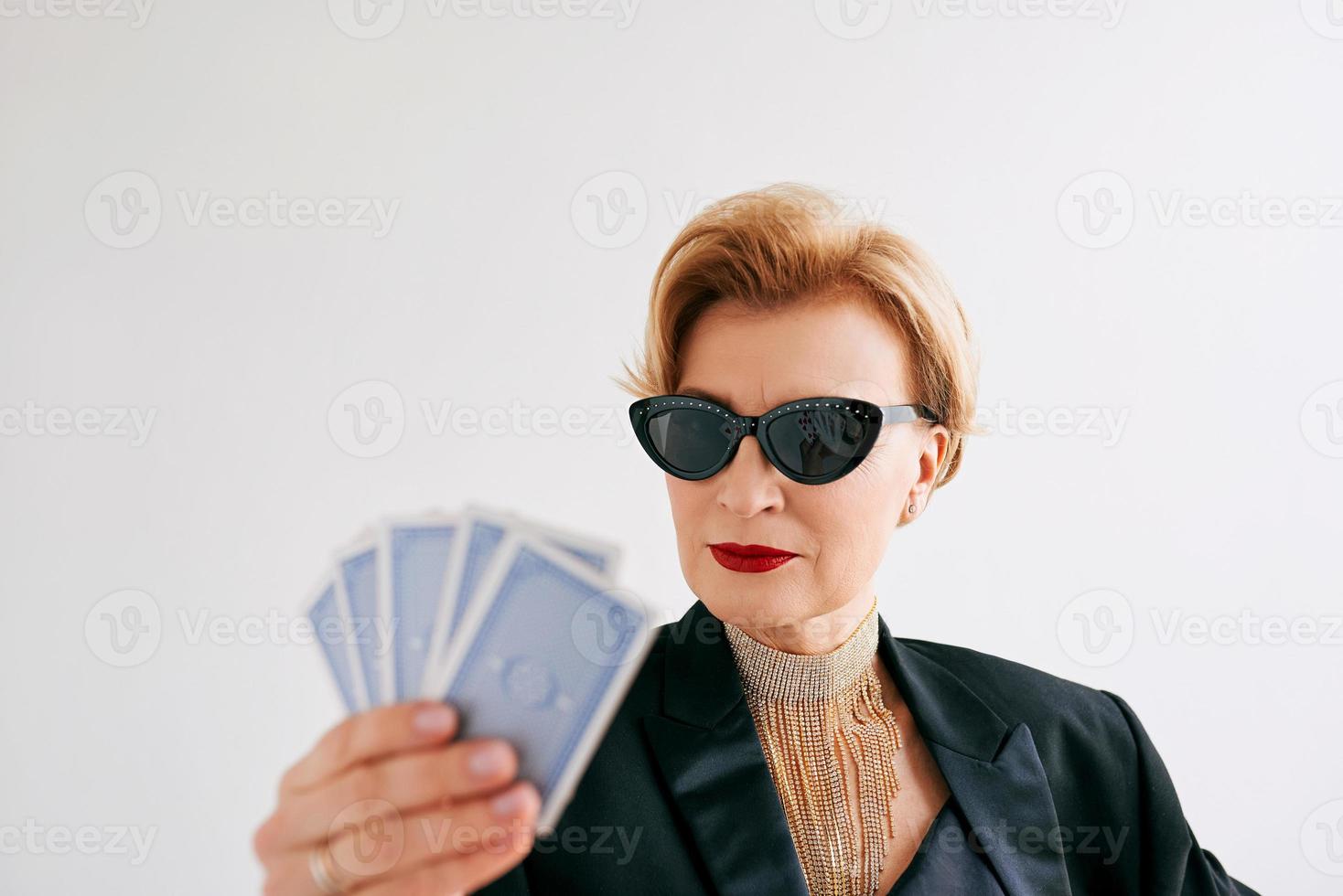 mujer madura y elegante con esmoquin negro y gafas de sol en el casino. juegos de azar, moda, cara de póquer, escalera real, concepto de hobby. foto