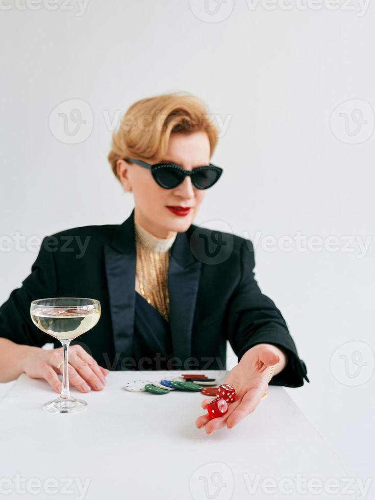 mature stylish woman in black tuxedo and sunglasses with dices in casino. Gambling, fashion, hobby concept. photo