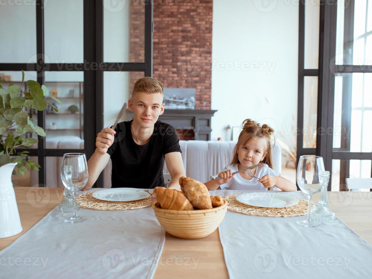 caucasian funny cute siblings -little girl with older brother in dining room in modern loft interior. Family, lifestyle and eating concept photo