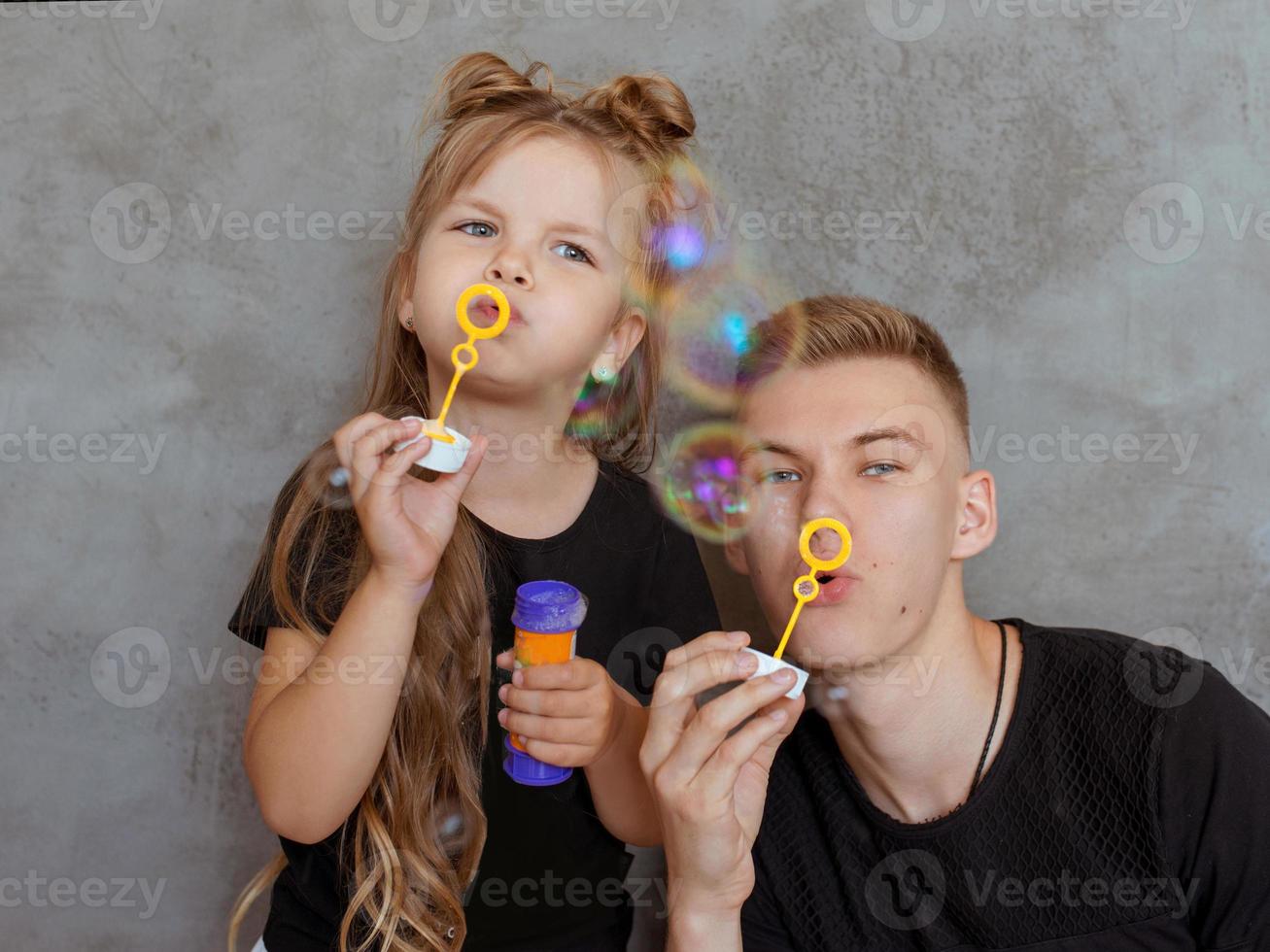 caucasian siblings - teenager boy brother and little girl sister with bubbles in modern loft interior on gray cement background photo