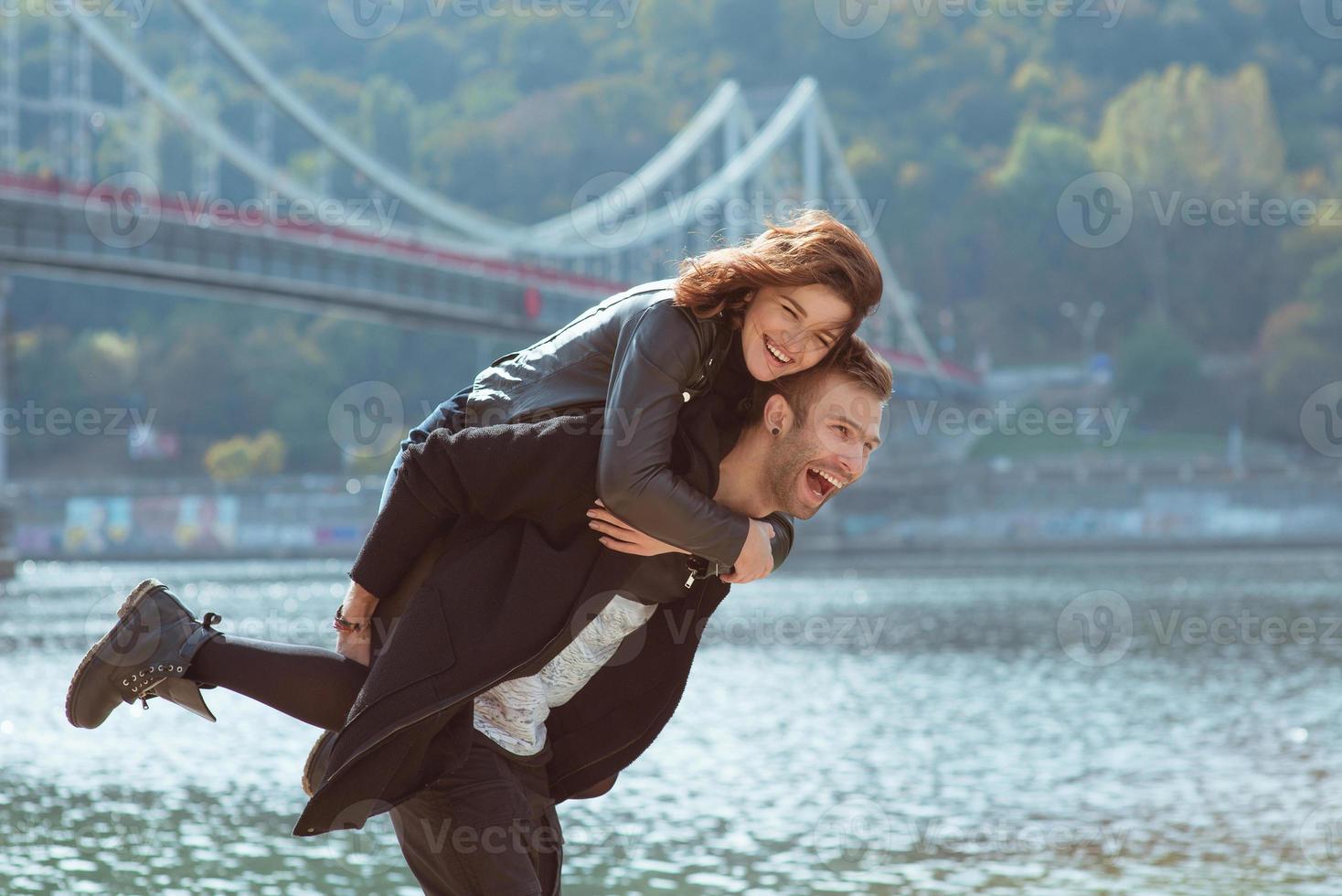hermosa increíble divertida alegre pareja joven abrazándose al aire libre junto al río en el fondo del puente. novia y novio. concepto de familia, amor y amistad foto