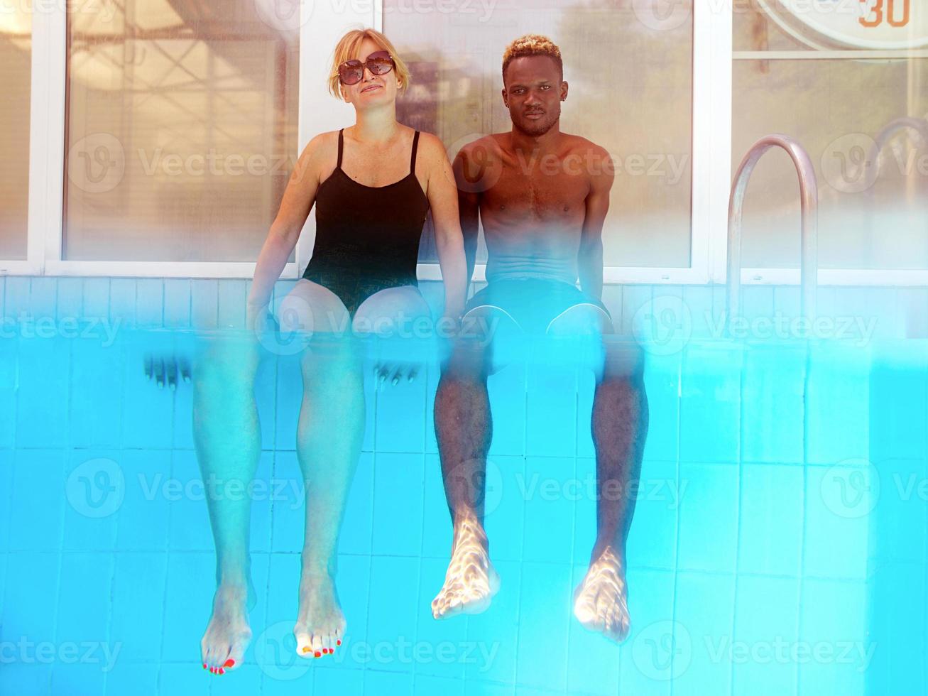 African American man with caucasian woman sitting on the edge of swimming pool. Summer. Vacation, international, and sport concept. photo