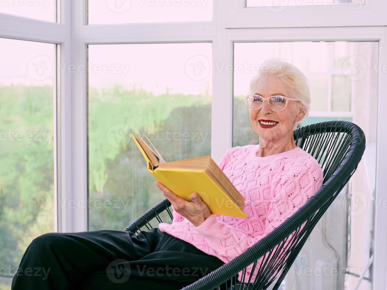 Senior stylish woman sitting on terrace reading book. Education, hobby concept photo