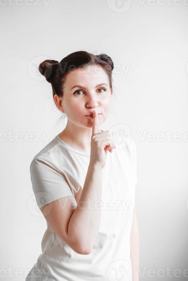Portrait woman with pigtails holding forefinger on her lips while standing over white backgrounnd. Copy, empty space photo