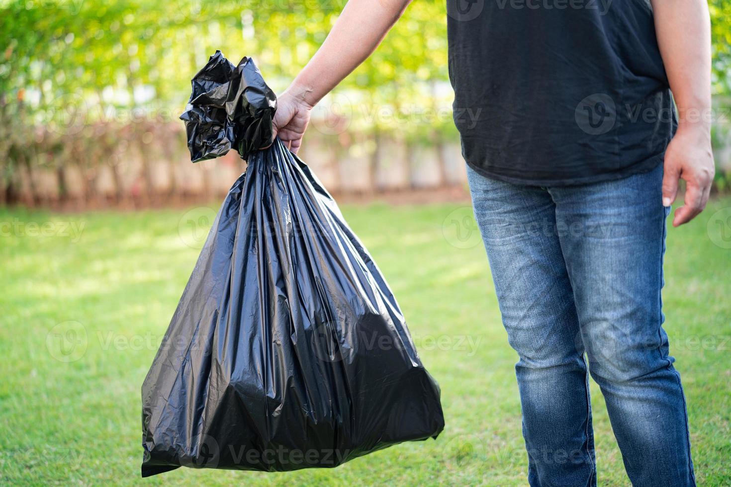 Woman holding black plastic trash bin bags of garbage on the pavement