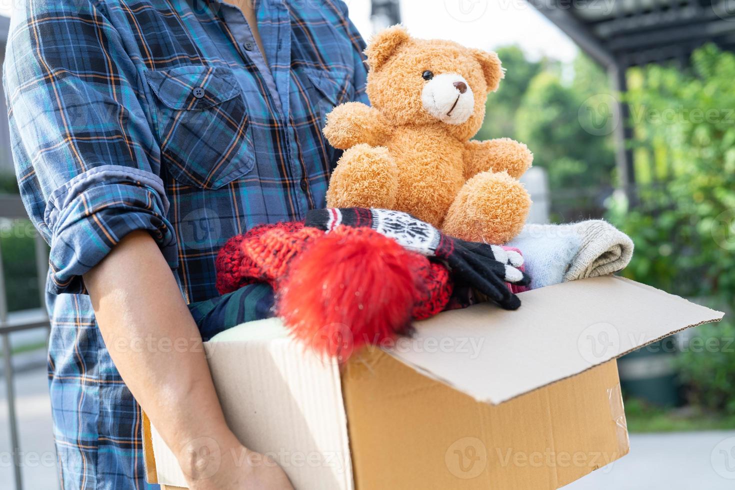 sosteniendo una caja de donación de ropa con ropa usada y muñecas en casa para apoyar la ayuda a los pobres del mundo. foto