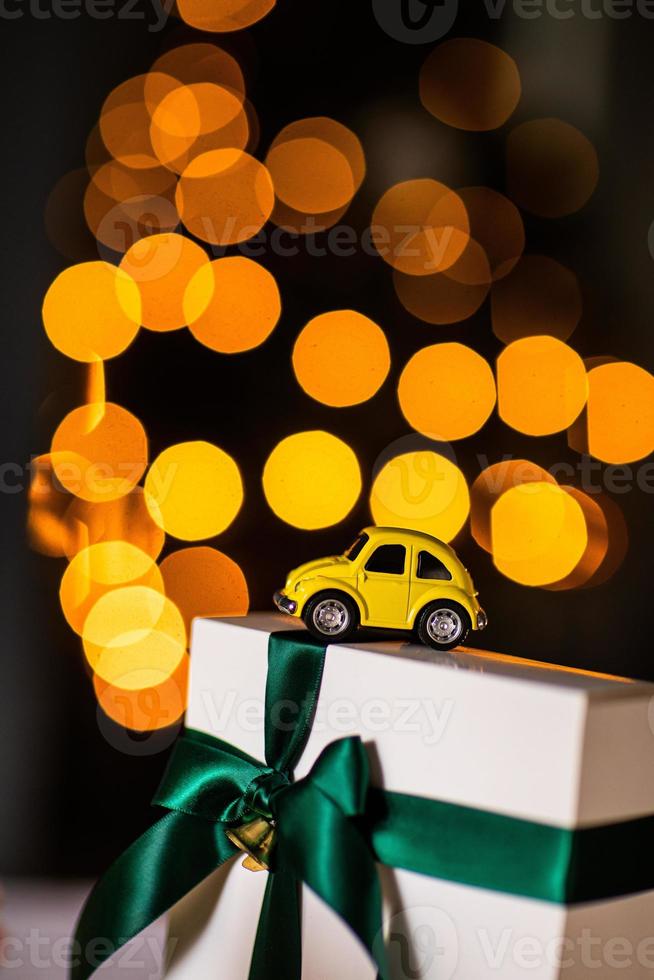 yellow small retro toy car on white gift with green ribbon on a Christmas yellow bokeh background. Delivery. New Year, Christmas, Valentines Day, World Womens Day, Sale concept. photo