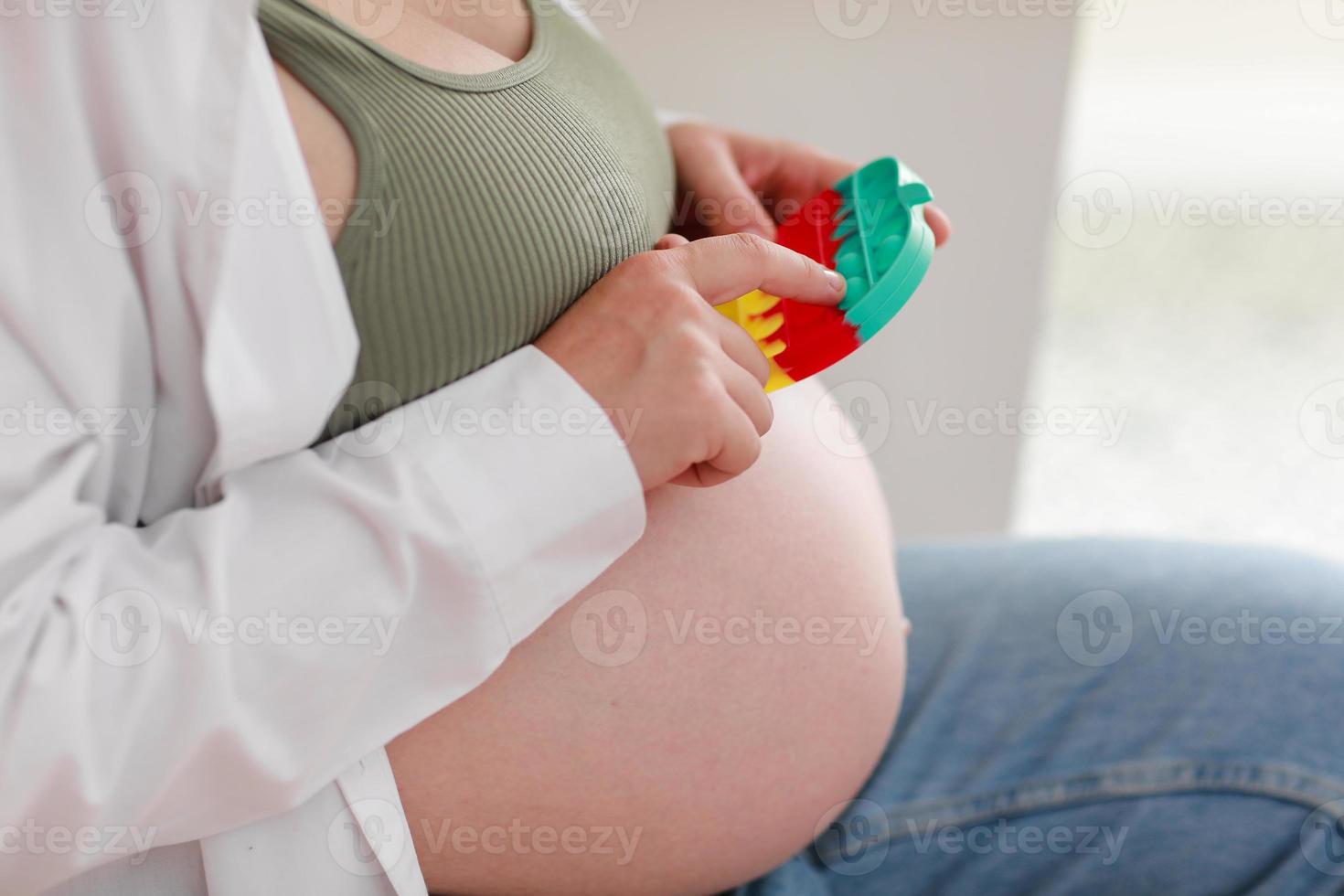 mujer embarazada con embarazo avanzado de barriga grande está usando poppit de juguete antiestrés y sentada en una silla en casa. Ansiedad y nerviosismo antes del parto. Embarazo saludable y feliz maternidad. foto