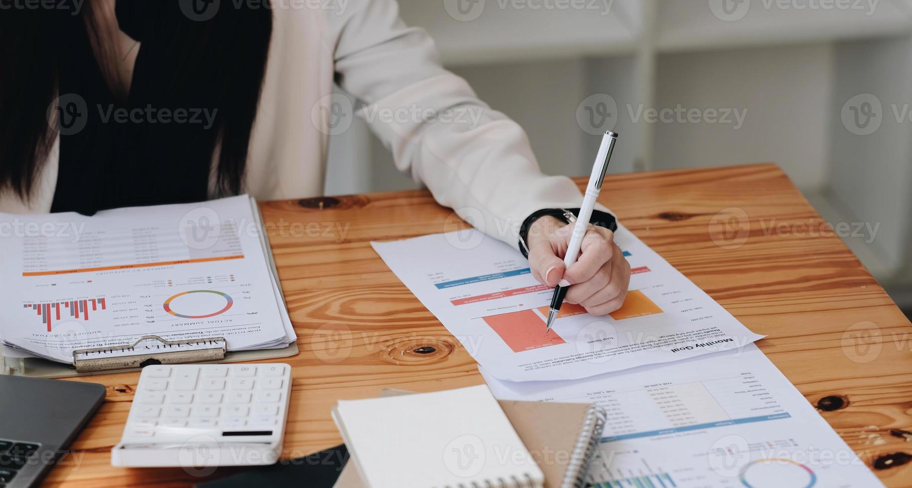 Close up Businesswoman hand holding pen and pointing at financial paperwork, financial charts to analyze profit concept photo