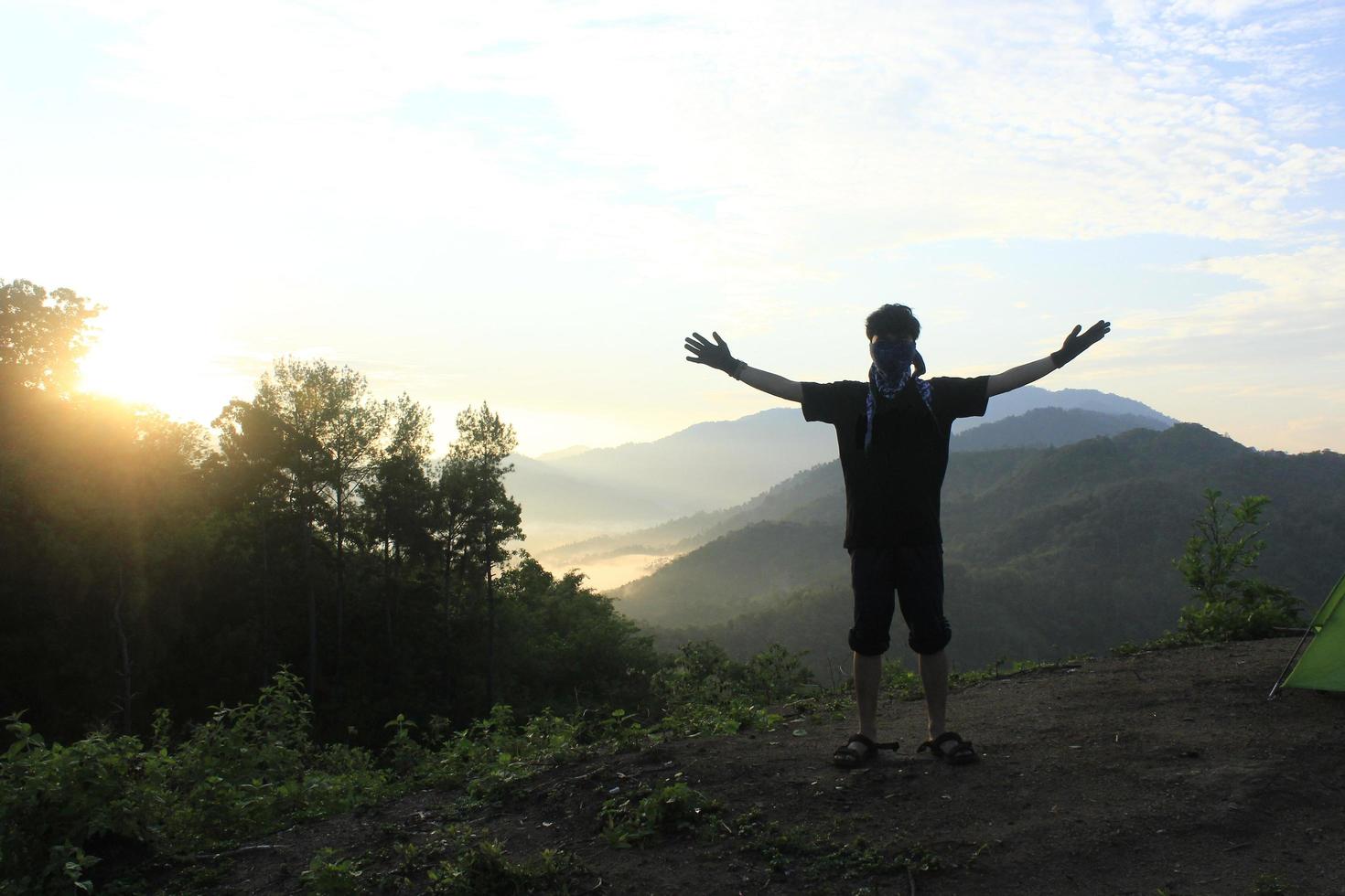 traveler hiking in the hills on blue sky background, traveler lifted his hands up photo