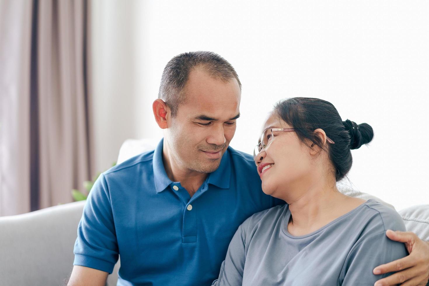 Portrait of Asian mature couple sitting in the living room. wife and husband hugging, holding hand with happiness and cheerful. Love, safety, and insurance family concept photo