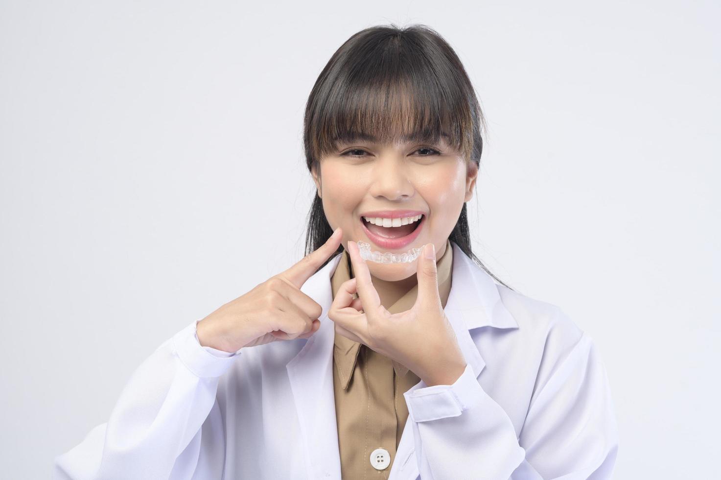 Young female dentist holding invisalign braces over white background studio, dental healthcare and Orthodontic concept. photo