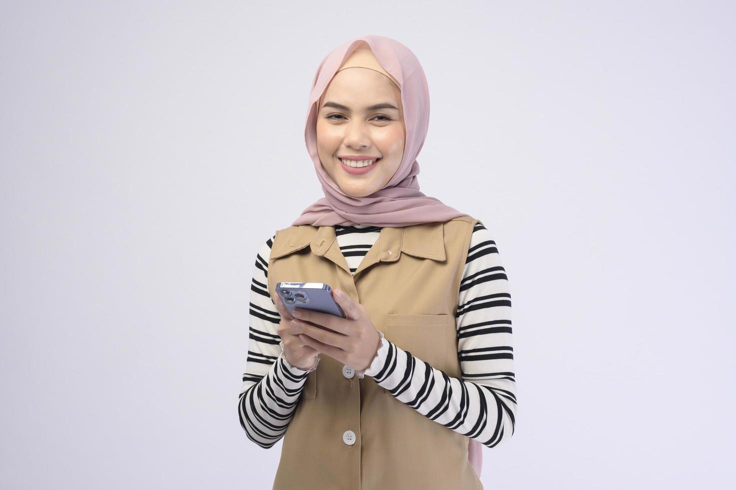 Portrait of beautiful woman with hijab using cellphone on white background photo