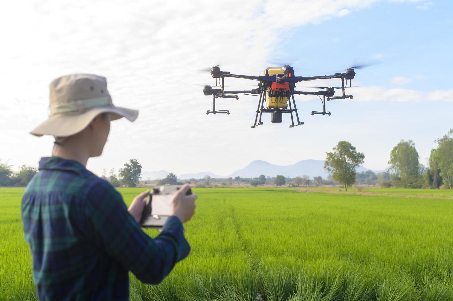 Young smart farmer controlling drone spraying fertilizer and pesticide over farmland,High technology innovations and smart farming photo