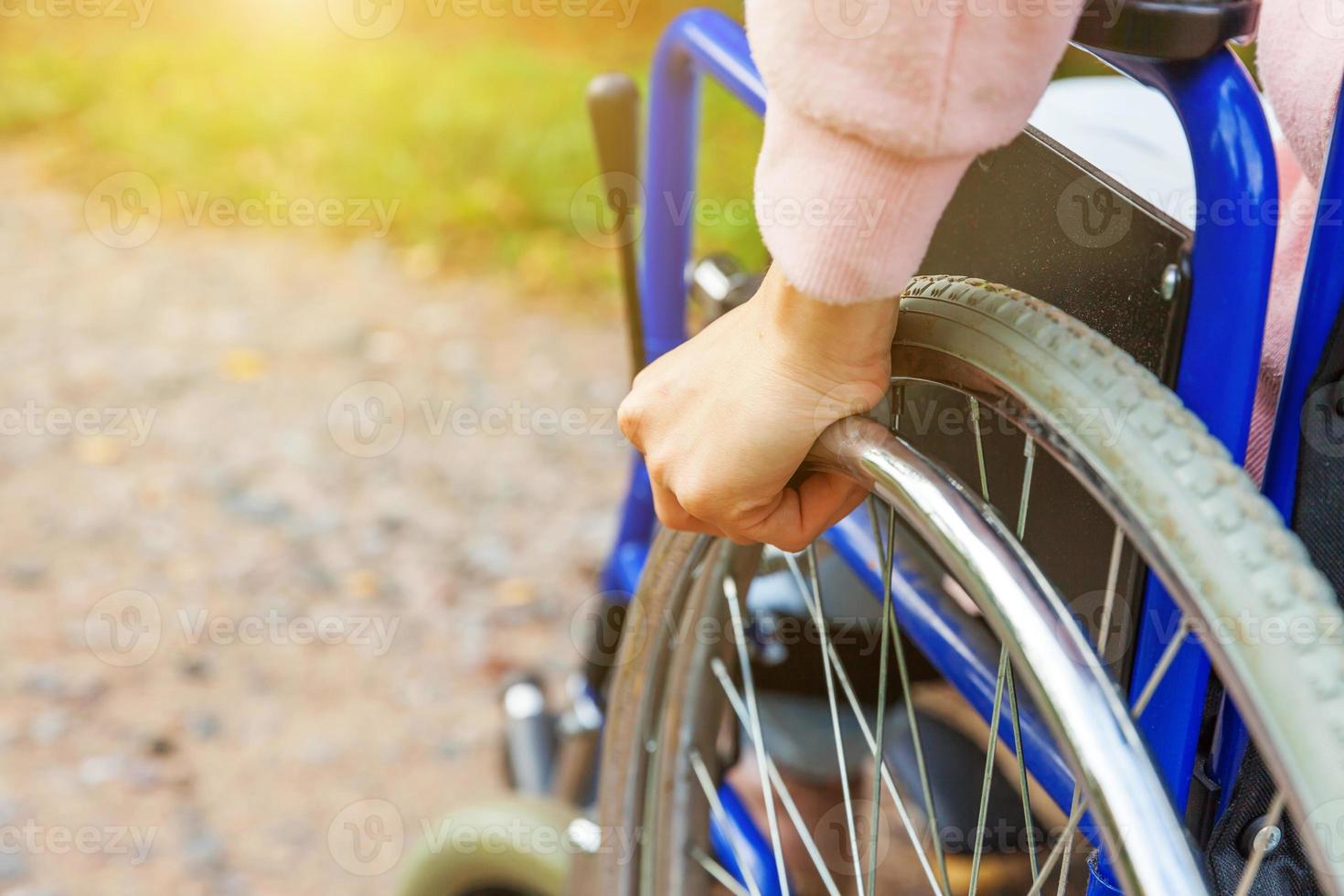 Hand handicap woman in wheelchair wheel on road in hospital park waiting for patient services. Unrecognizable paralyzed girl in invalid chair for disabled people outdoors. Rehabilitation concept. photo