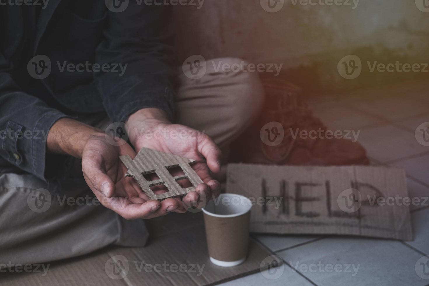 Homeless adult man sitting on the street in the shadow of the building and begging for help and money with sign.  Homeless concept. photo