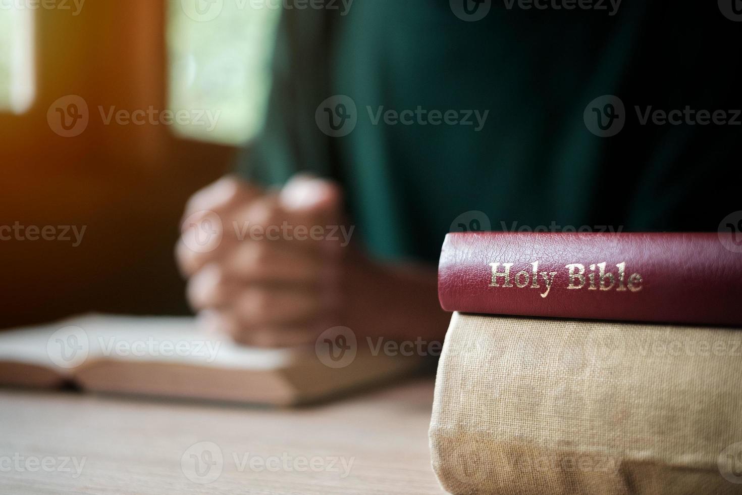 Man with Bible praying, hands clasped together on her Bible on wooden table. photo