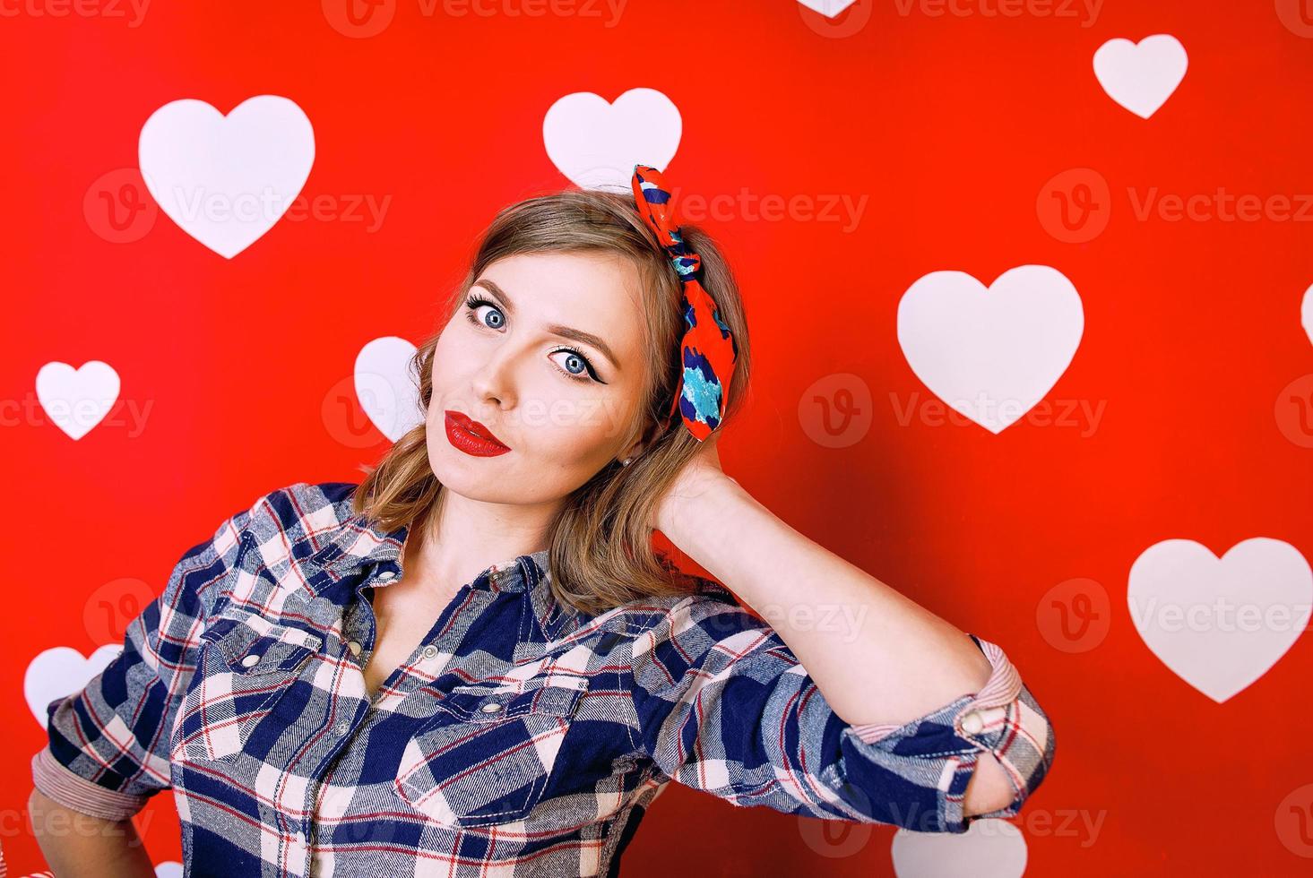 Beautiful young woman in pin-up style on red with white hearts background photo