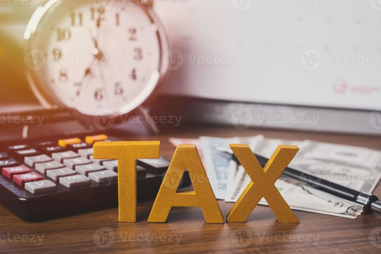 Debt collection and tax season concept. The word tax written in wooden block letters with calculator, money, clock, pen, background, Time to pay concept photo