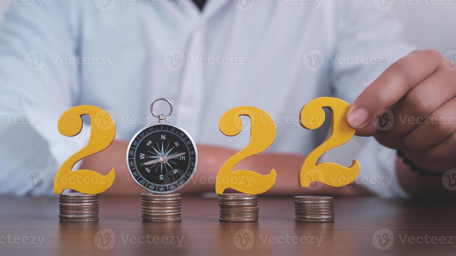 Man hands putting gold wooden number 2022 on the stack of coins compass, financial direction 2022. Tax payment, 2022 new year saving money and financial planning concept photo