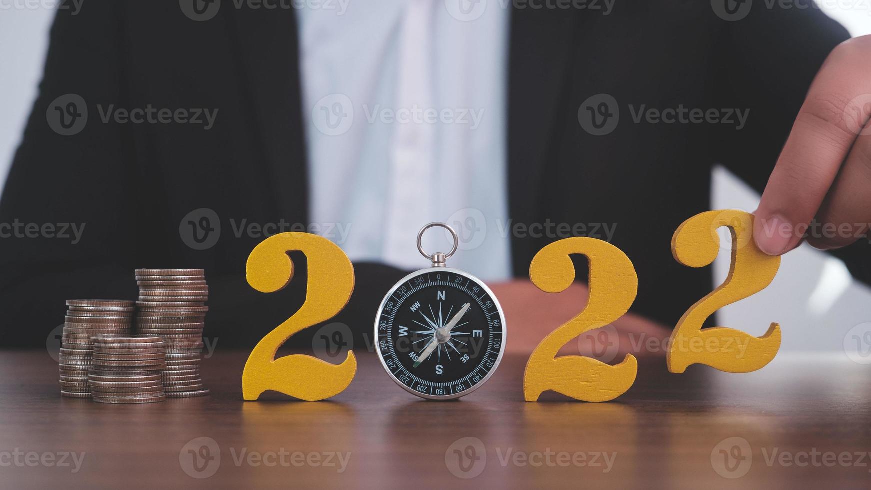 Man hands putting gold wooden number 2022 on the stack of coins compass, financial direction 2022. Tax payment, 2022 new year saving money and financial planning concept photo