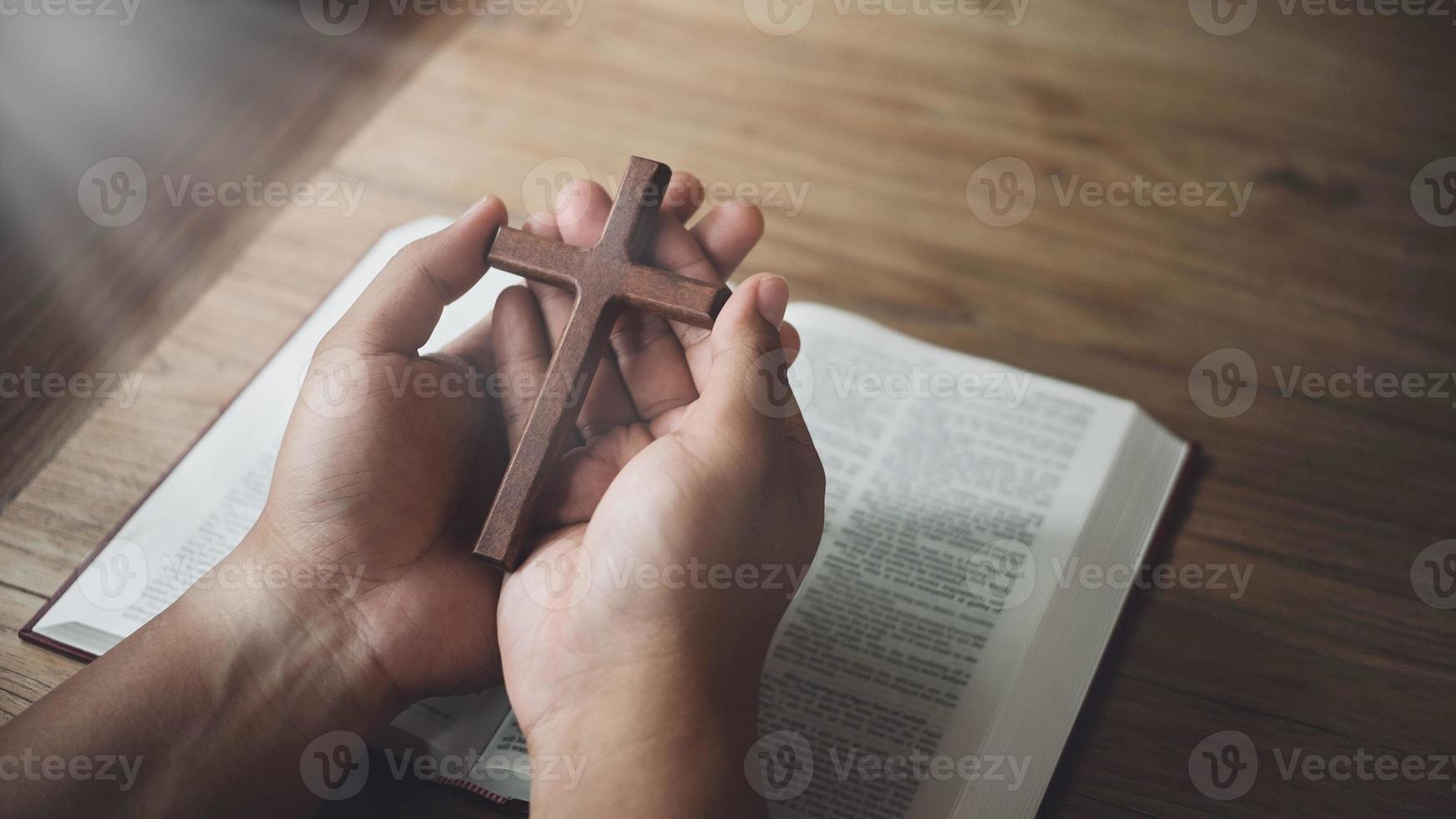 hombre sosteniendo una cruz de madera en las manos sobre la biblia y la luz divina. concepto de religión. foto