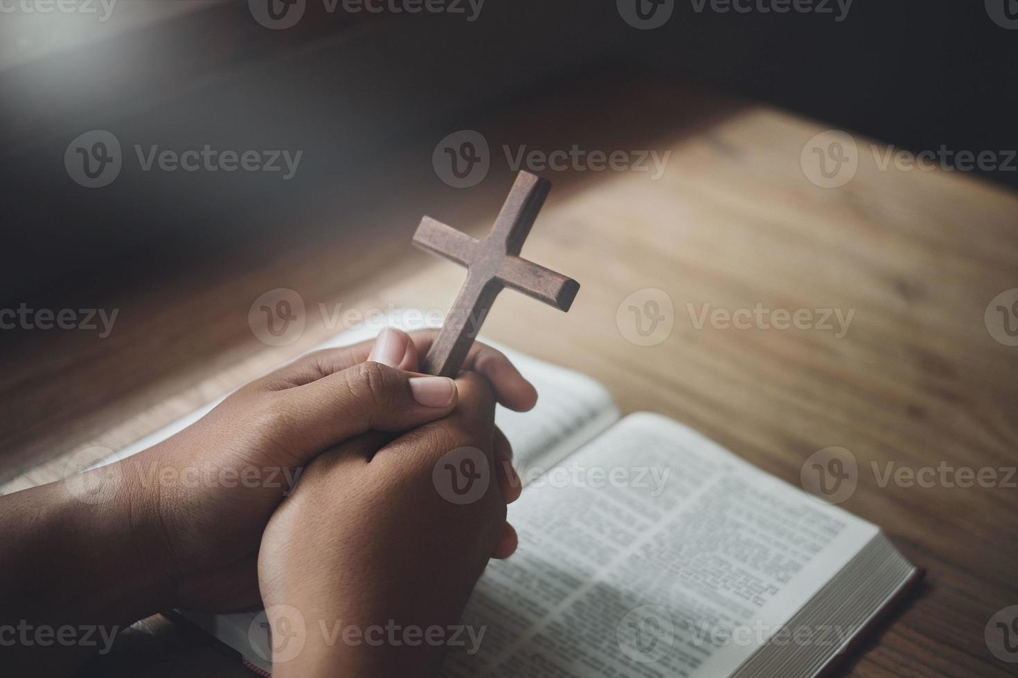 Man holding wooden cross in hands on bible and divine light. Religion concept. photo