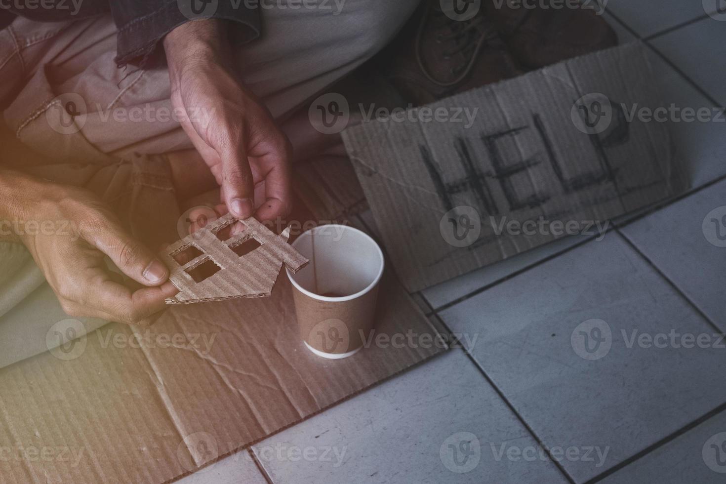 Homeless adult man sitting on the street in the shadow of the building and begging for help and money with sign.  Homeless concept. photo