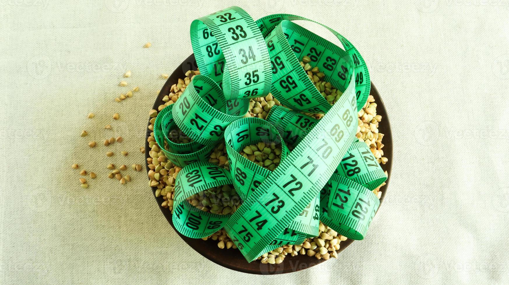 Green measuring tape on a background of raw buckwheat in a dish, concept of diet and healthy nutrition. Vegan organic food concept. Quarantine weight loss. Copy space for text. Top view, flat lay photo