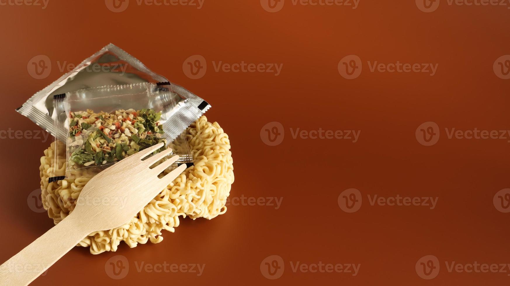Raw instant noodles in the shape of a circle with a wooden fork and aromatic seasonings and butter. pasta, for the preparation of which it is enough to pour boiling water and wait a few minutes. photo